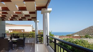 Un balcón con mesa y sillas, vista al mar y un paisaje montañoso.