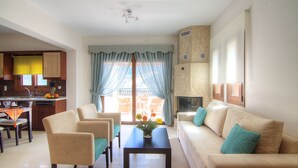 Una sala de estar moderna con un sofá, sillas, una mesa de centro y una cocina visible a través de un vidrio.