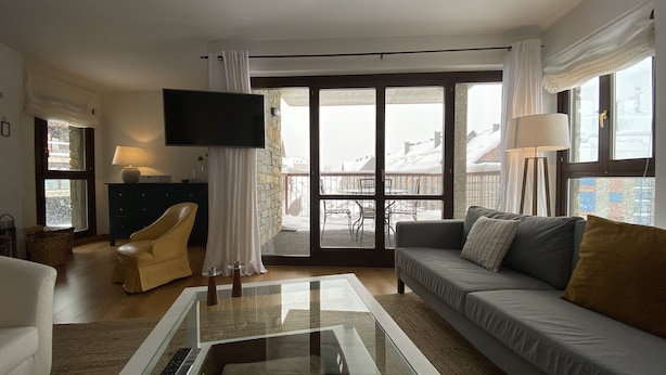 Un salon moderne avec un canapé, une table basse, un téléviseur et un balcon offrant une vue sur les immeubles.