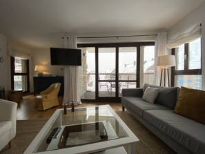 Ett modernt vardagsrum med en soffa, ett soffbord, en tv och en balkong med utsikt över byggnader.