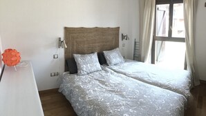 Une chambre à coucher avec un grand lit, deux lampes de chevet, un luminaire fixé au mur et une fenêtre avec des rideaux.