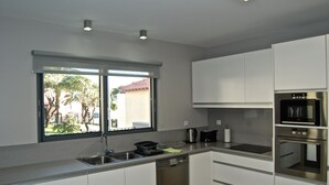 A modern kitchen with white cabinets, stainless steel appliances, and a window providing a view of the outside. - Casa da Praia Calheta - Moradia (Calheta)