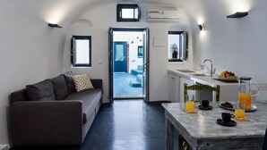 Un espace de vie compact comprenant un canapé, une table à manger avec des éléments pour le petit-déjeuner, et une vue sur une pièce bleue par une porte ouverte.