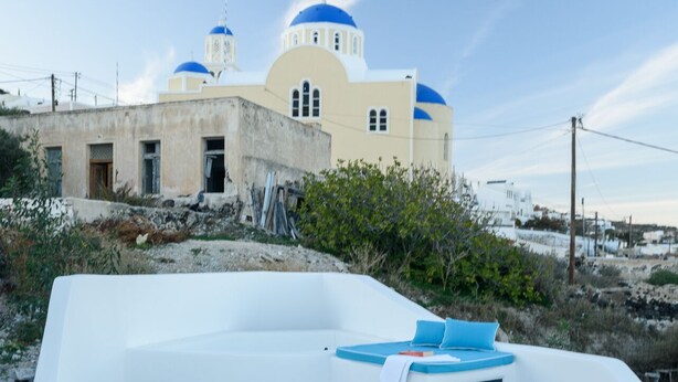 Un espace extérieur ensoleillé, aménagé avec une table et des chaises, un banc rembourré, et offrant une vue sur un bâtiment doté de coupoles bleues.