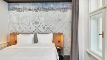Una habitación de hotel con una cama grande, un cabecero con lámparas fijadas a la pared, una mesita y una ventana con cortinas.