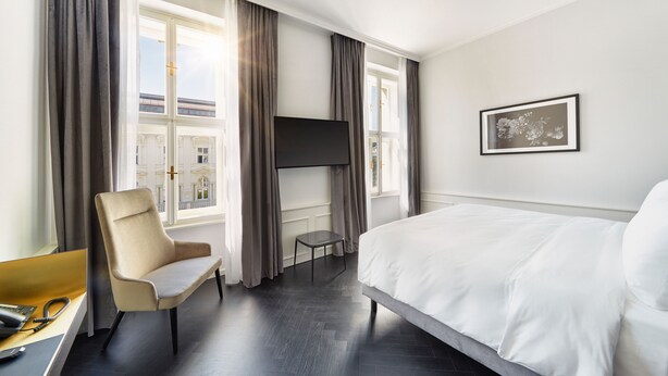 Una habitación de hotel con cama, una silla, televisión y ventana con cortinas.