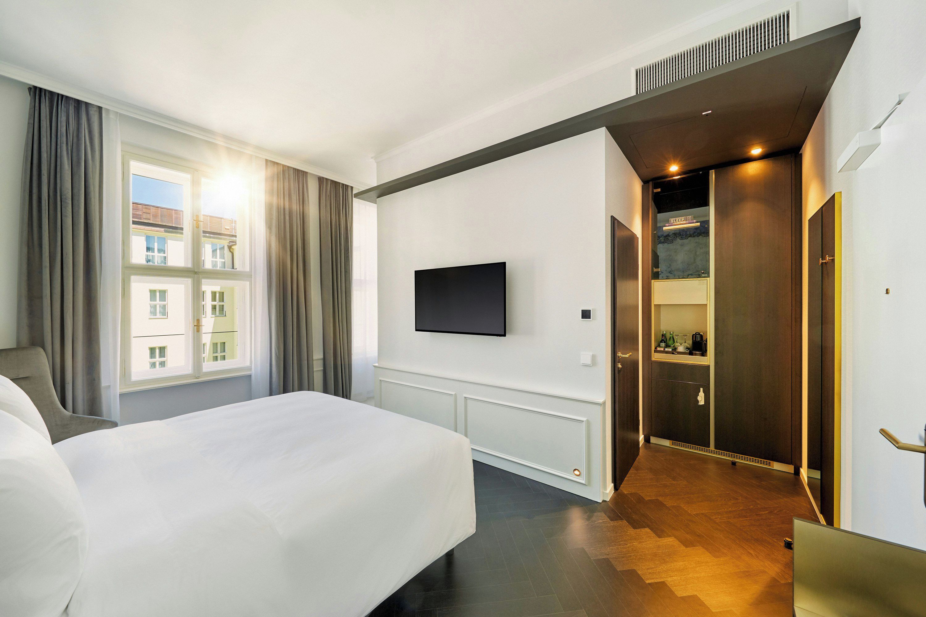 A hotel room with a large bed, a flat-screen TV mounted on the wall, and a view of the outside through the window.