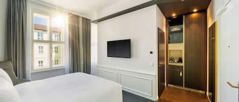 A hotel room with a large bed, a flat-screen TV mounted on the wall, and a view of the outside through the window.