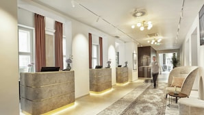 Zona de recepción de un hotel con diseño moderno, que incluye un mostrador de recepción, un área de espera con sofá y suelo alfombrado.