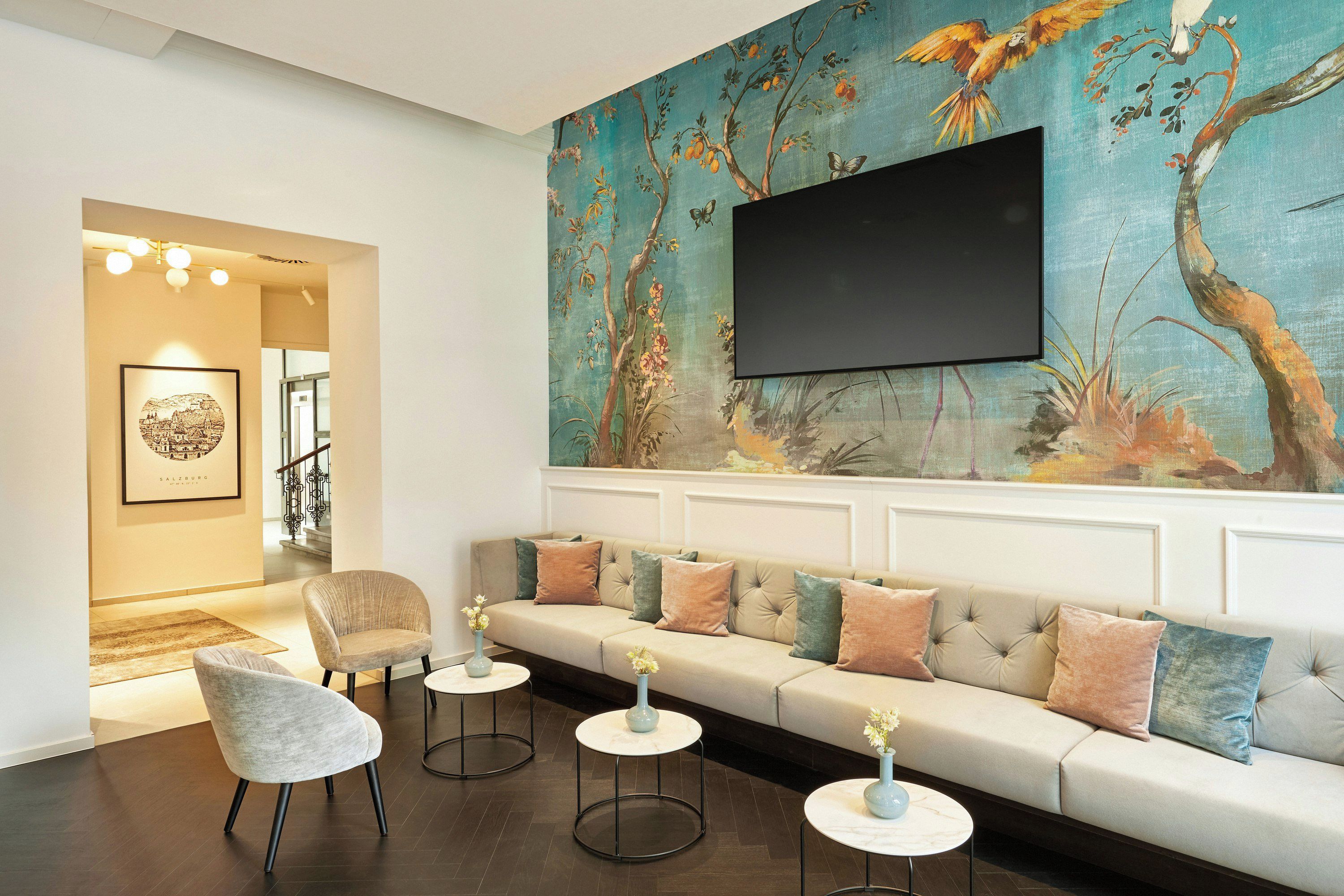 Een moderne woonkamer met een bank, fauteuils en een muurschildering van een televisiescherm.