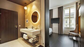 A modern bathroom with a double sink, a mirror with a circular light, and a towel rack.