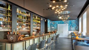 A bar area with a long counter, multiple shelves with bottles, and bar stools.