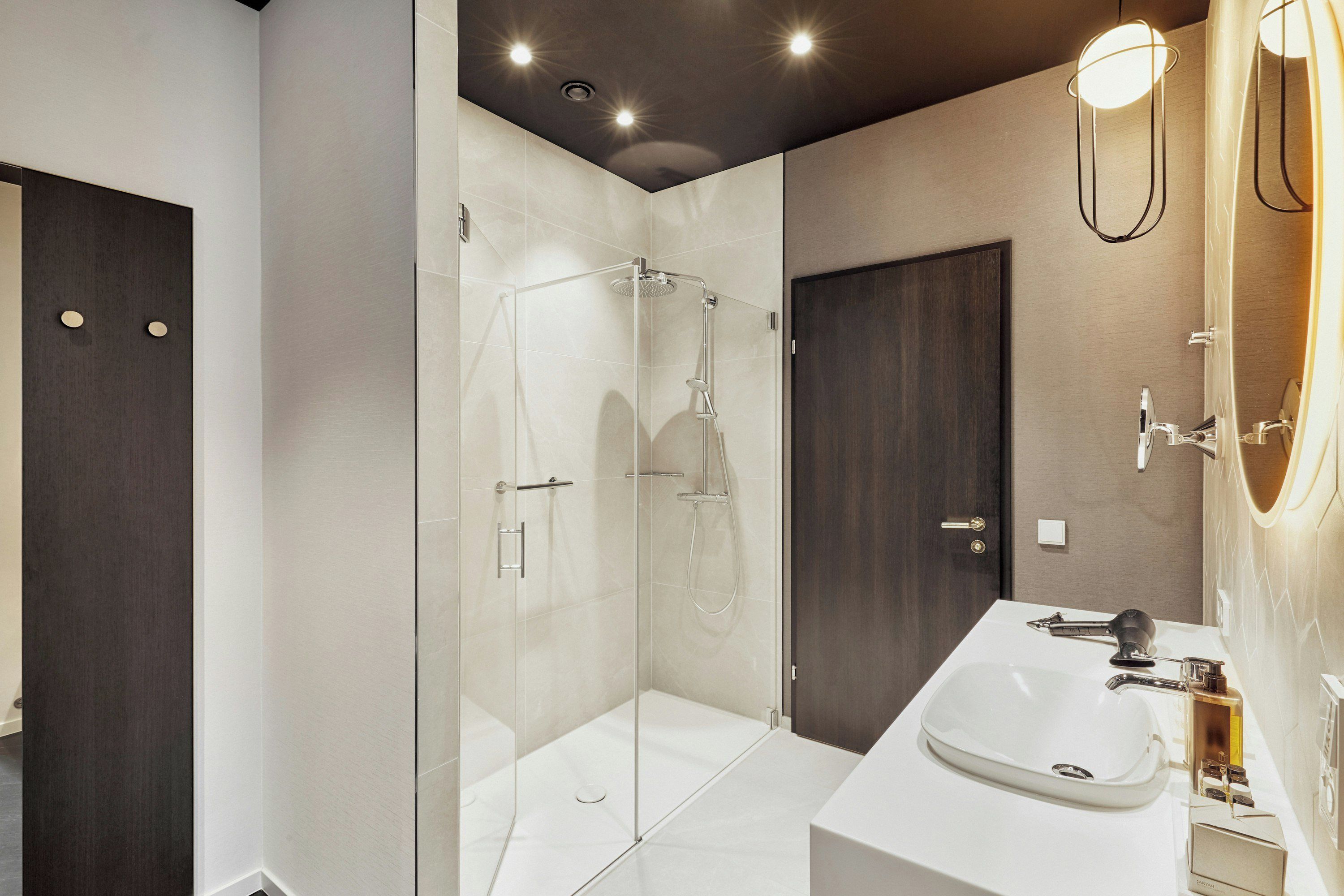 A modern bathroom with a glass-enclosed shower, a white sink, and a dark wooden door.