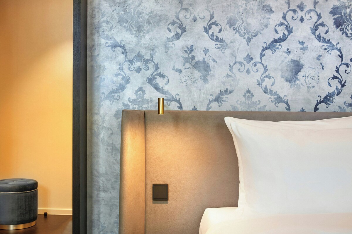 Una habitación de hotel con cama, mesita de noche y papel tapiz estampado.