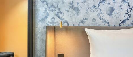 Una habitación de hotel con cama, mesita de noche y papel tapiz estampado.