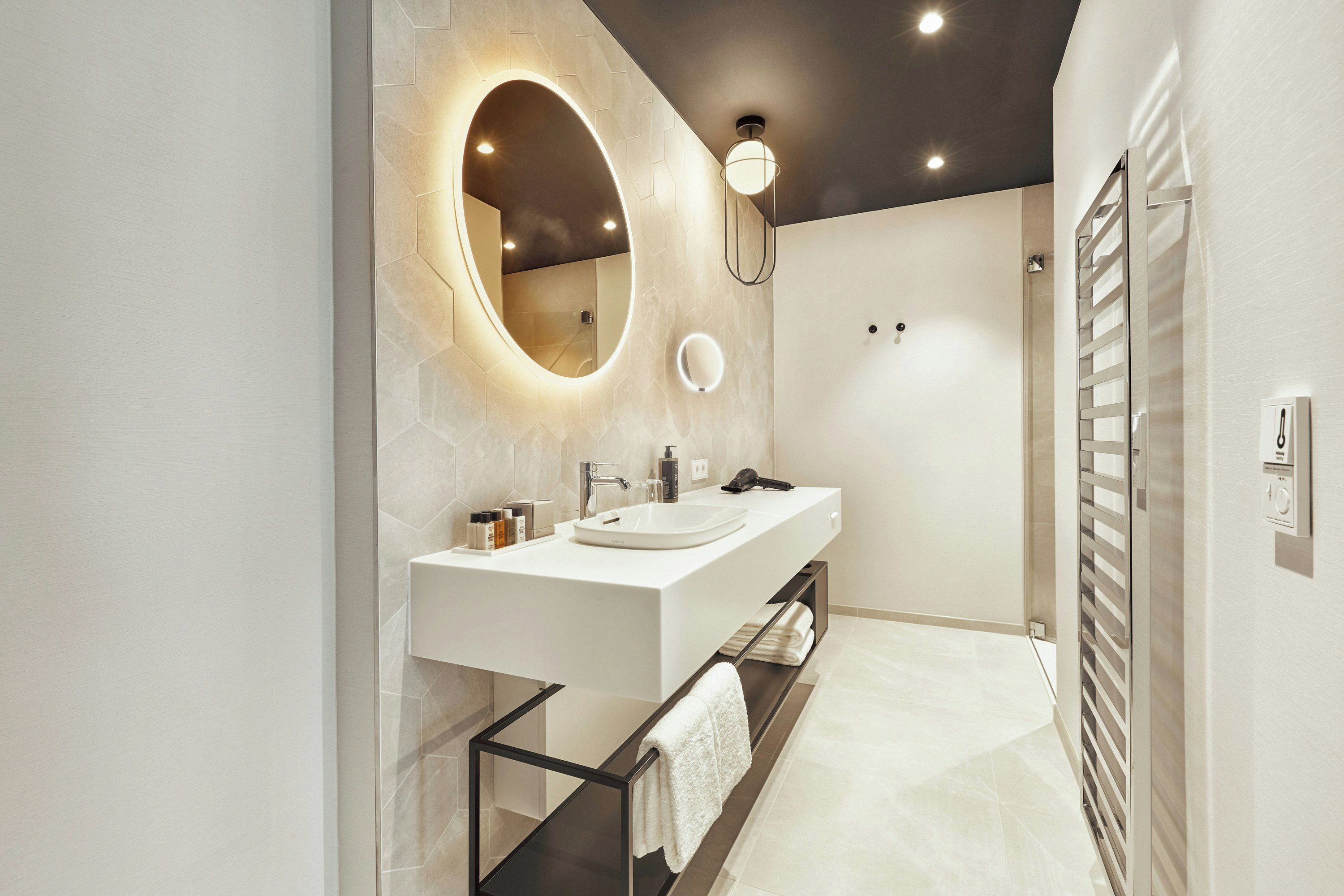 A modern bathroom with a white vanity, a large mirror, and a towel rack.