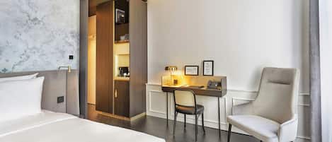 A hotel room with a bed, a desk with a chair, a wardrobe, and a large artwork on the wall.