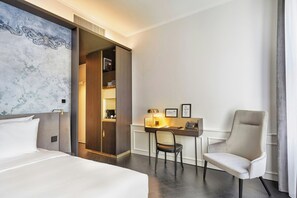 Habitación de hotel con cama, escritorio, silla, armario y una obra de arte grande en la pared.