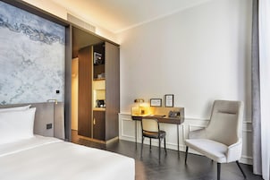 Habitación de hotel con cama, escritorio, silla, armario y una obra de arte grande en la pared.