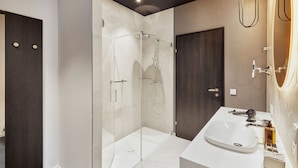 Un baño moderno con ducha de vidrio, un lavamanos blanco y una puerta de madera oscura.