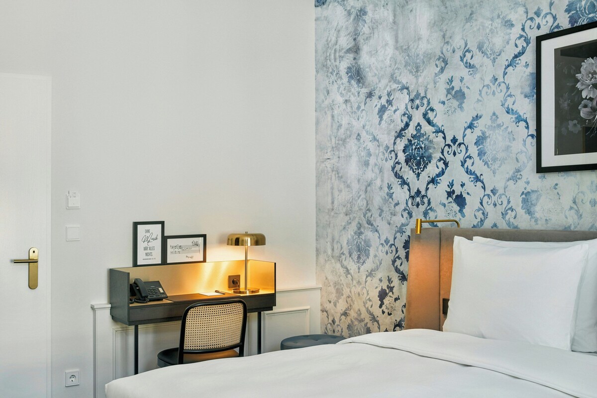Habitación de hotel con cama, escritorio con teléfono, una silla y un papel tapiz con diseño.