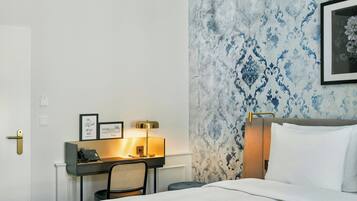 A hotel room with a bed, a desk with a telephone, a chair, and a wall with a patterned wallpaper.