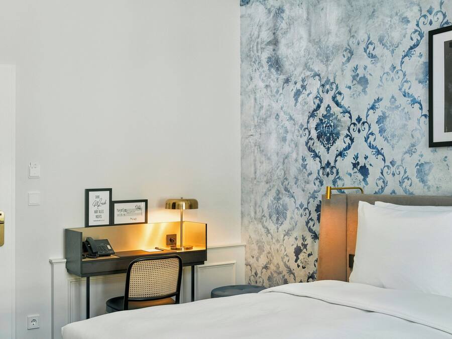 Een hotelkamer met een bed, een bureau met telefoon, een stoel en een wand met behang.