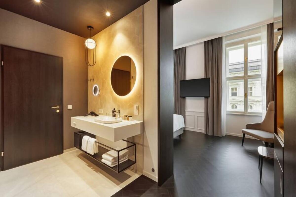 Un baño moderno con un espejo grande, una lámpara redonda y un lavamanos separado.