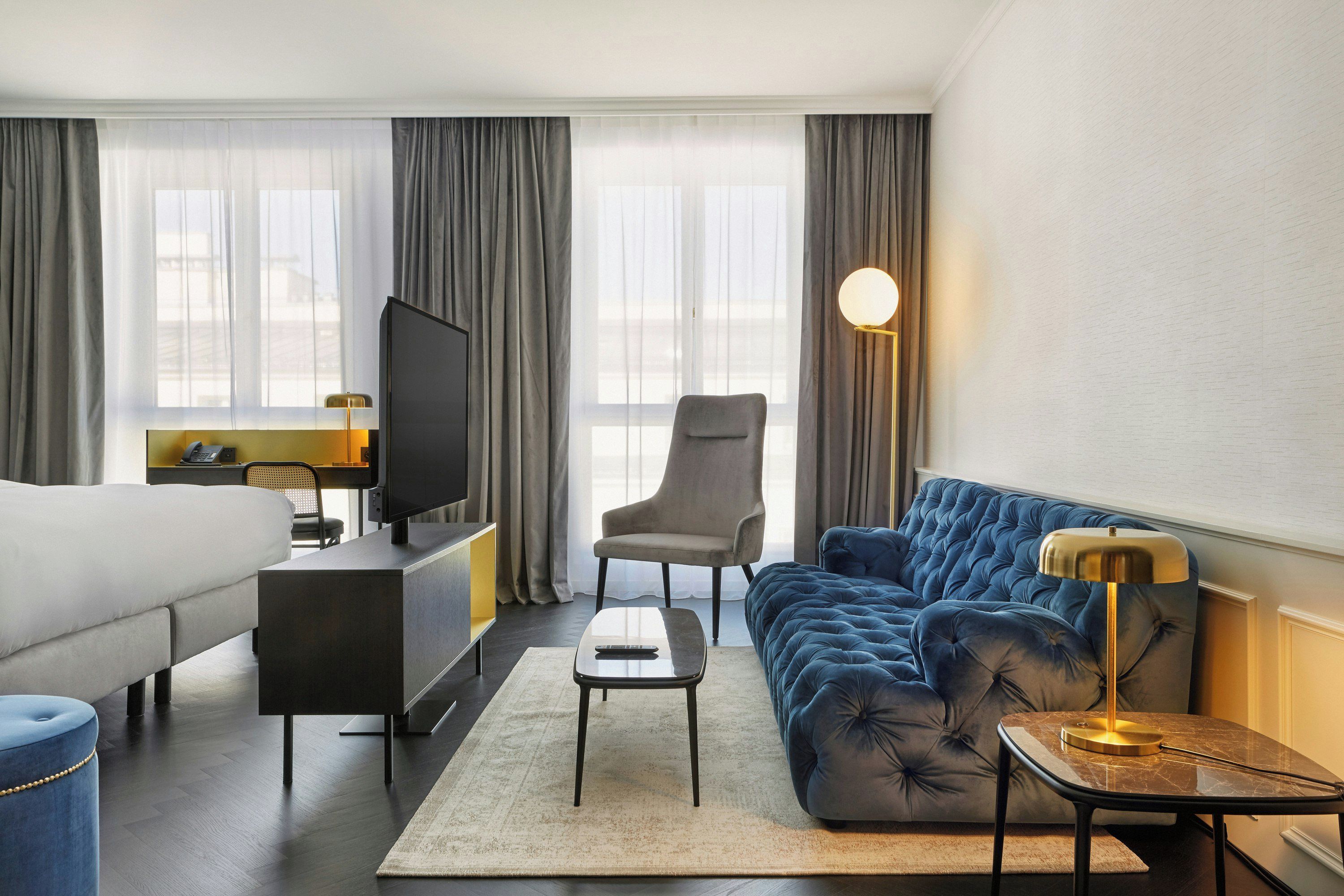 Une chambre d’hôtel comprenant un lit, un canapé, un bureau avec une télévision, une chaise et une lampe.