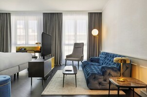 Una habitación de hotel con cama, sofá, escritorio con televisor, silla y lámpara.