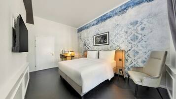 A hotel room with a bed, bedside tables, a chair, a flat-screen TV, and a decorative wall.