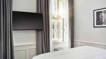 A hotel room with a bed, a flat-screen TV mounted on the wall, a window with curtains, and a framed picture on the wall.
