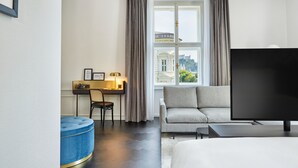 Habitación de hotel con sofá, televisor, escritorio con silla y ventana con cortinas.