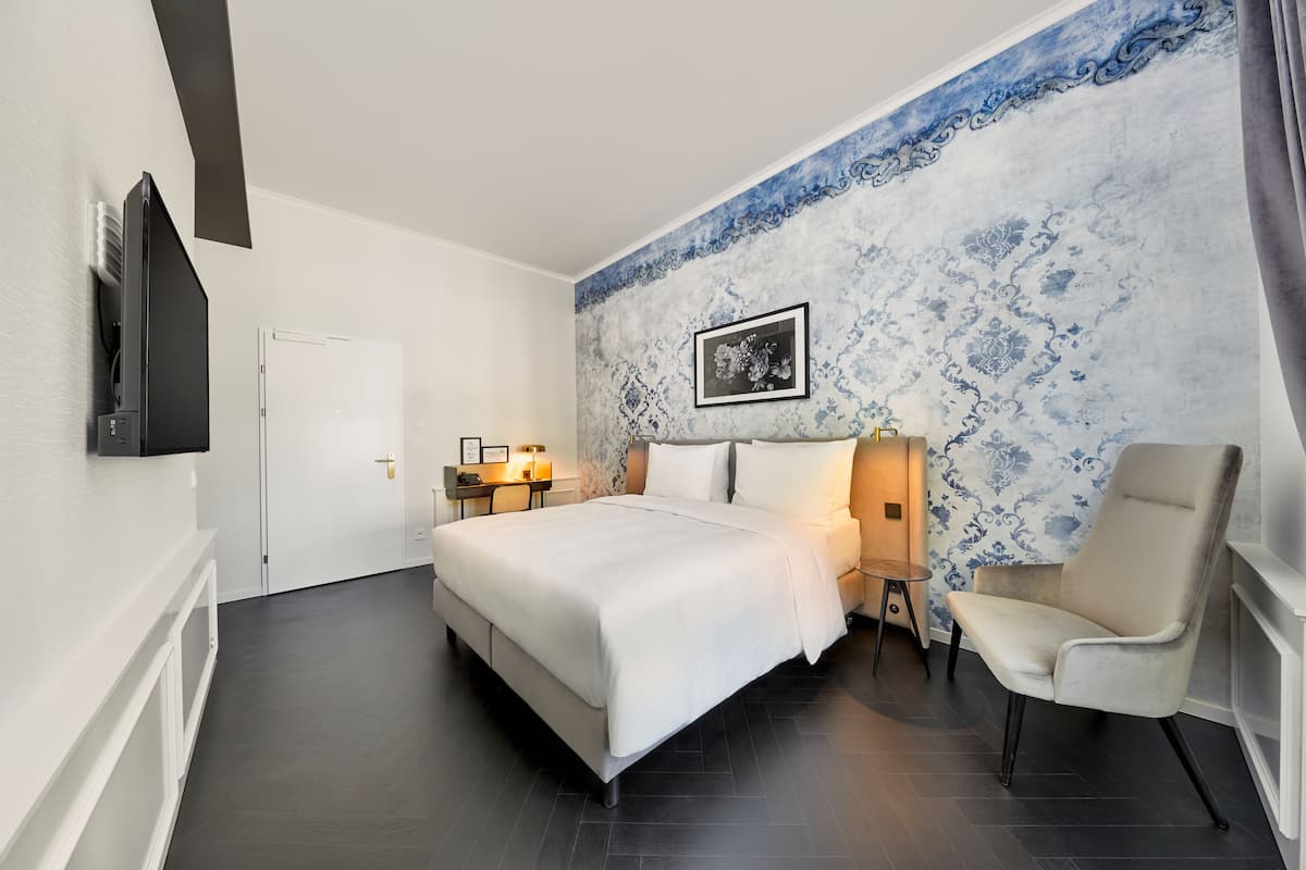 Una habitación de hotel moderna con una cama grande, una silla, un televisor y un detalle decorativo en la pared.