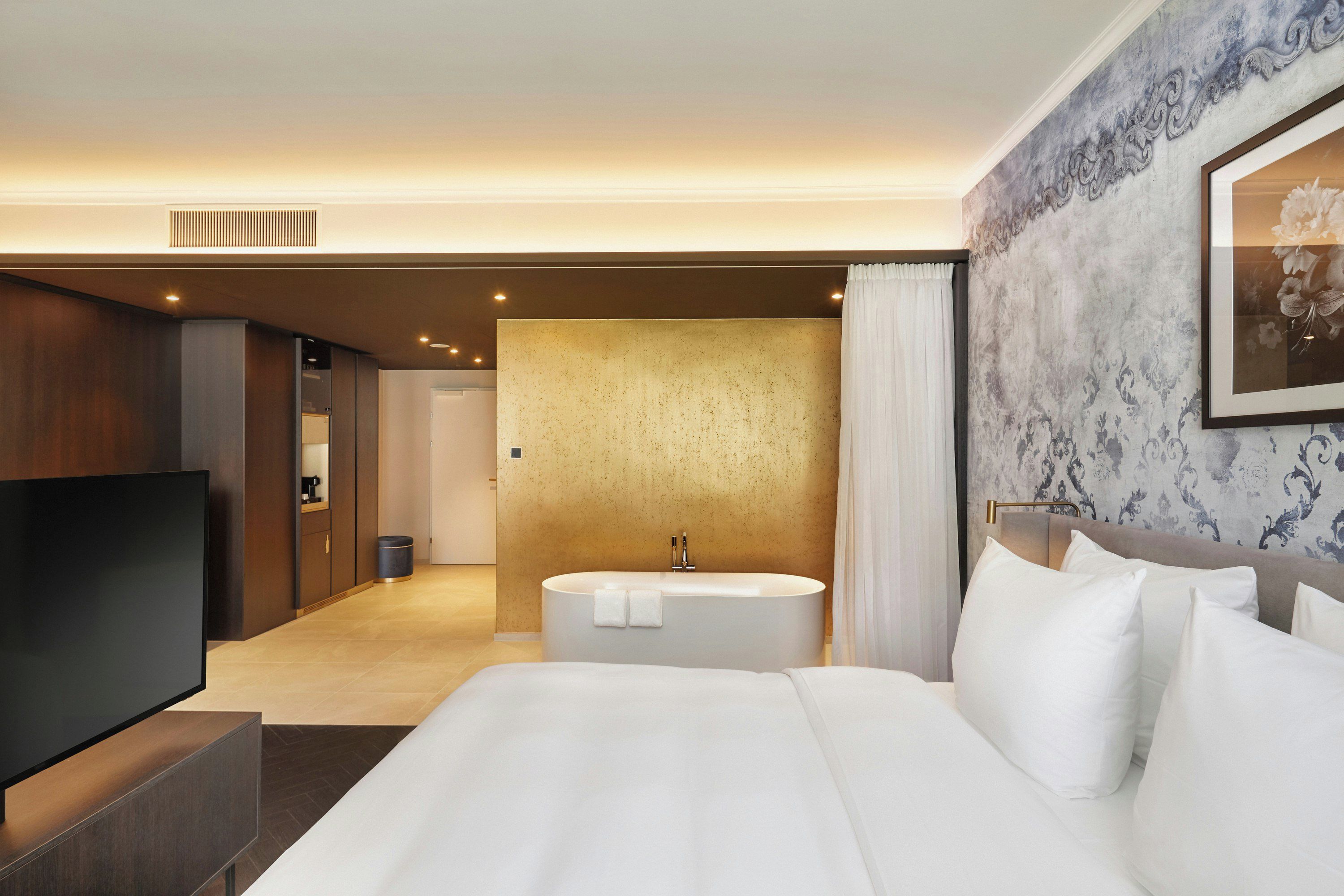 Habitación de hotel con una cama grande, un televisor de pantalla plana, una bañera redonda y un baño con espejo e inodoro.