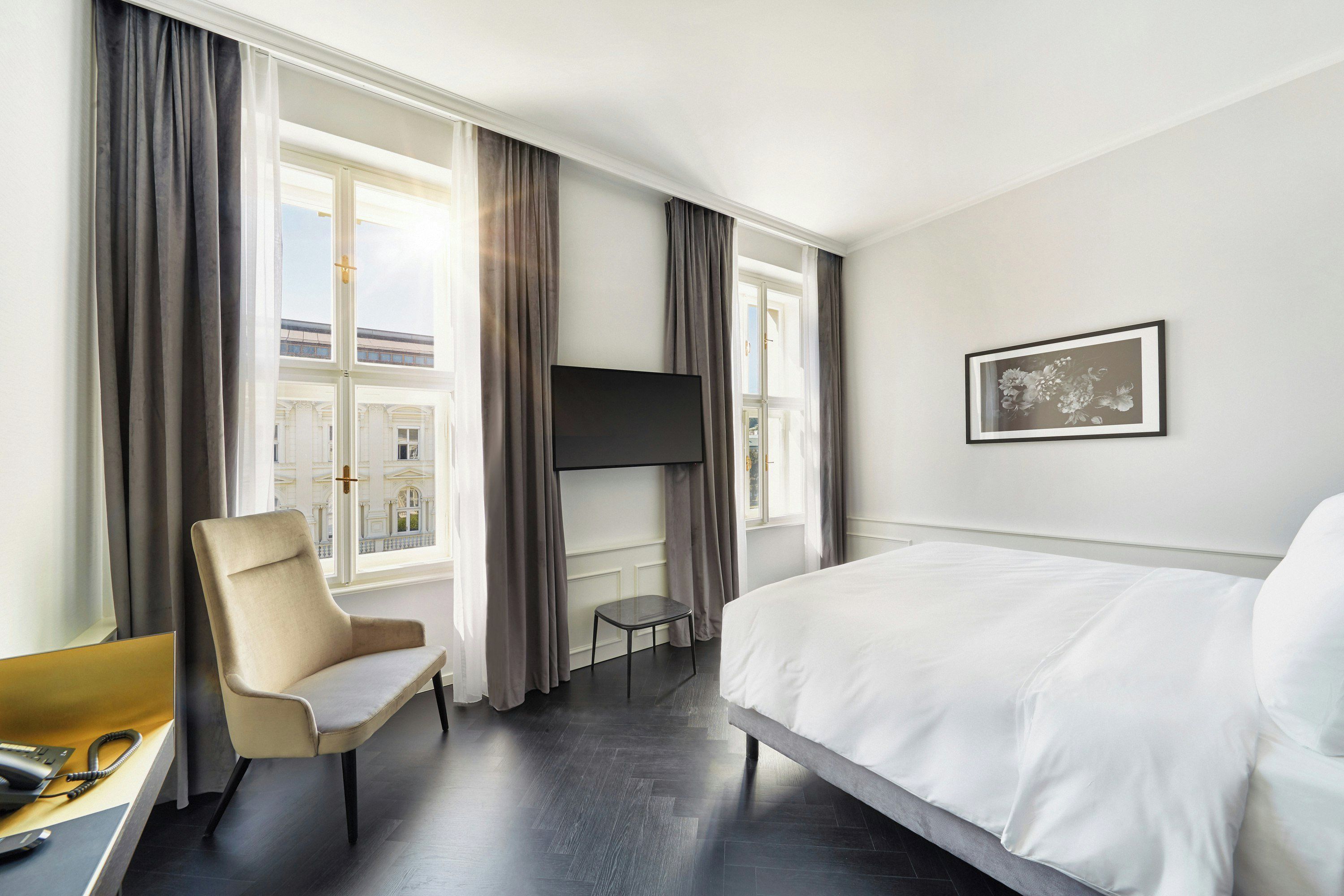 Ein Hotelzimmer mit Bett, Stuhl, Fernseher und einem fenster mit Vorhängen.