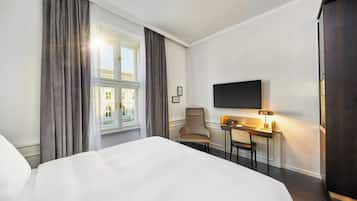 A hotel room with a bed, a desk with a chair, a television, and a window with curtains.