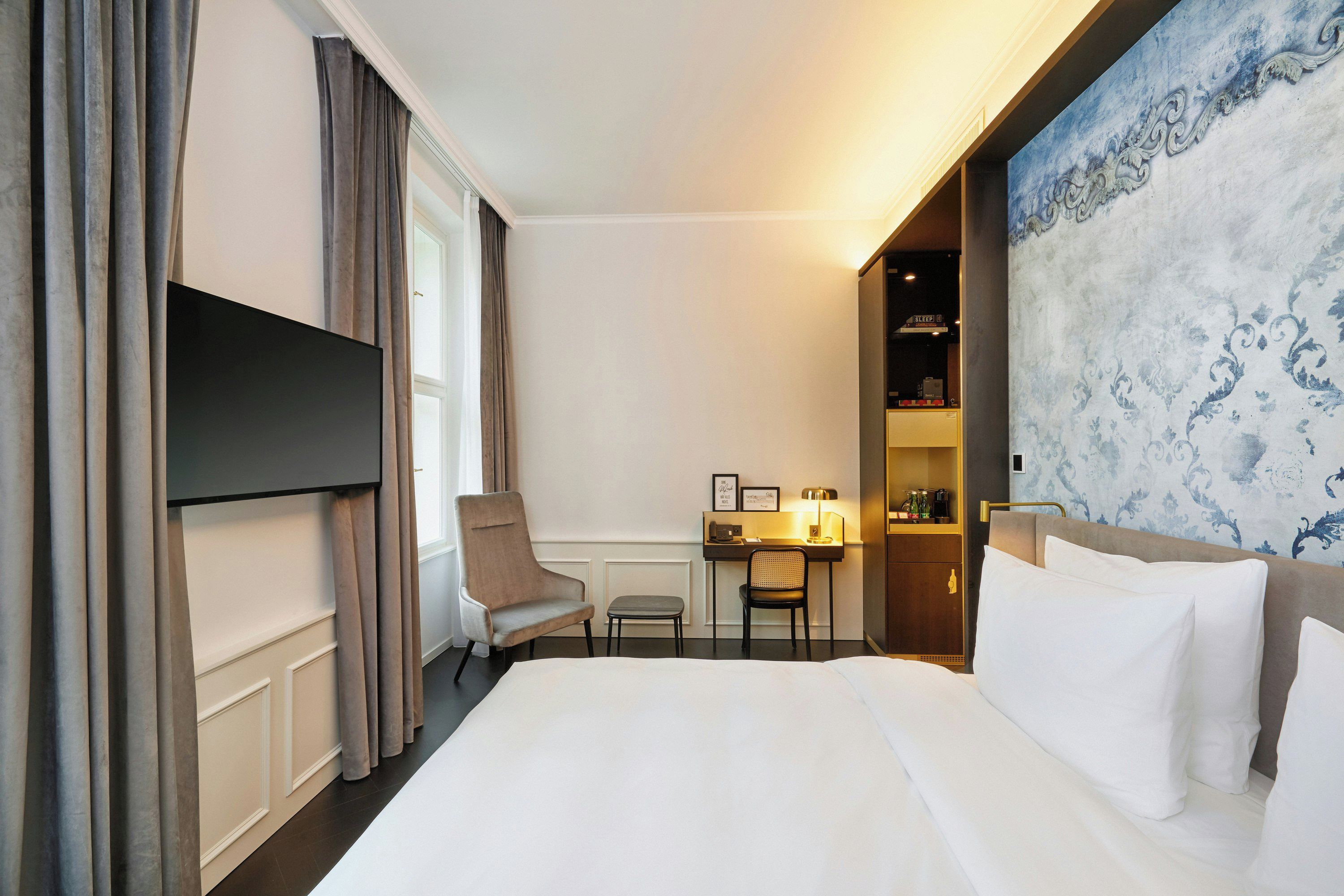 A hotel room with a bed, a desk, a chair, a TV, and a decorative wall.