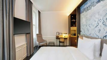 A hotel room with a bed, a desk, a chair, a TV, and a decorative wall.