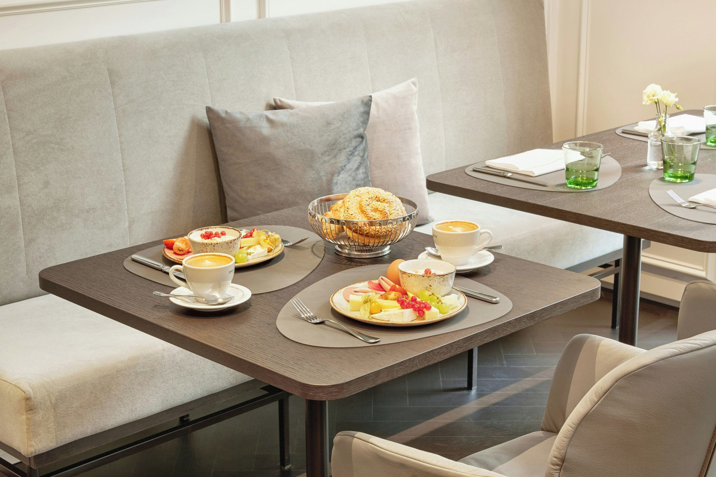 Un comedor con una mesa dispuesta para dos, que incluye platos de comida, un bol de pan y una taza de café.