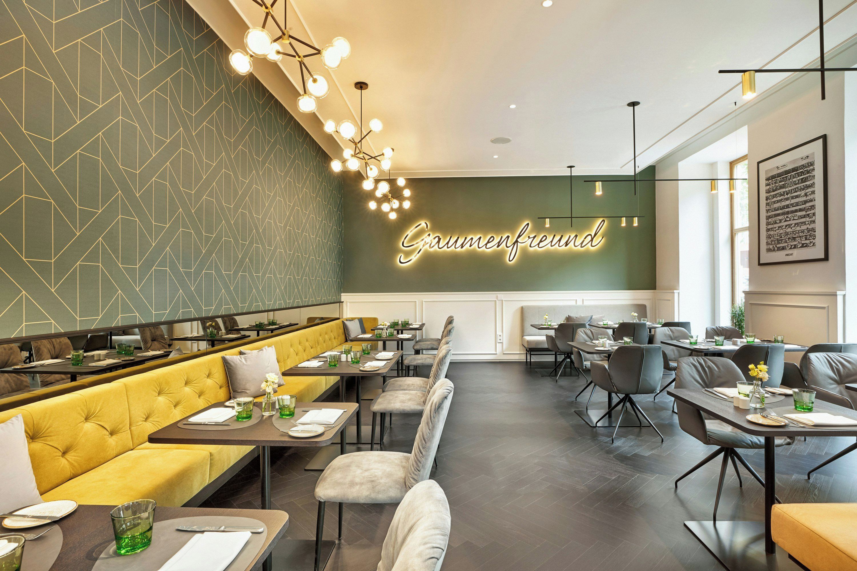 A restaurant interior with a geometric patterned wall, a neon sign reading 'Sauenfreund,' and a framed musical score on the wall.