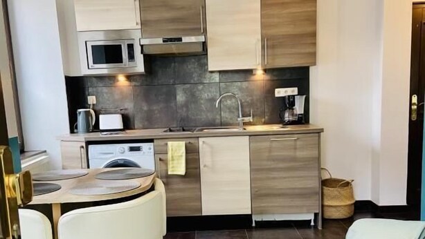 Una cocina compacta con electrodomésticos modernos, una zona de comedor con una mesa redonda y sillas, y una acogedora sala de estar con una pequeña mesa redonda y un tapete tejido.
