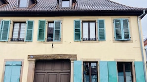 Un edificio con una puerta de madera grande, varias ventanas con contraventanas verdes y un tejado de tejas.