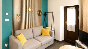 A modern living room with a grey sofa, yellow cushions, a wooden accent wall, a television, and a round wooden table.