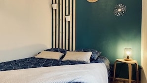 Un dormitorio con cama, mesita de noche con lámpara, aplique de pared y un adorno en la pared.