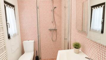 A bathroom with a white toilet, a shower with a glass door, a sink with a mirror, and a patterned floor.