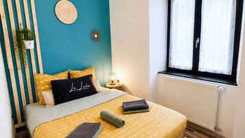 A bedroom with a bed, a window, a wall-mounted light fixture, and a potted plant.