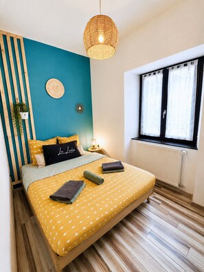 Une chambre à coucher avec un lit, une fenêtre, un luminaire fixé au mur et une plante en pot.