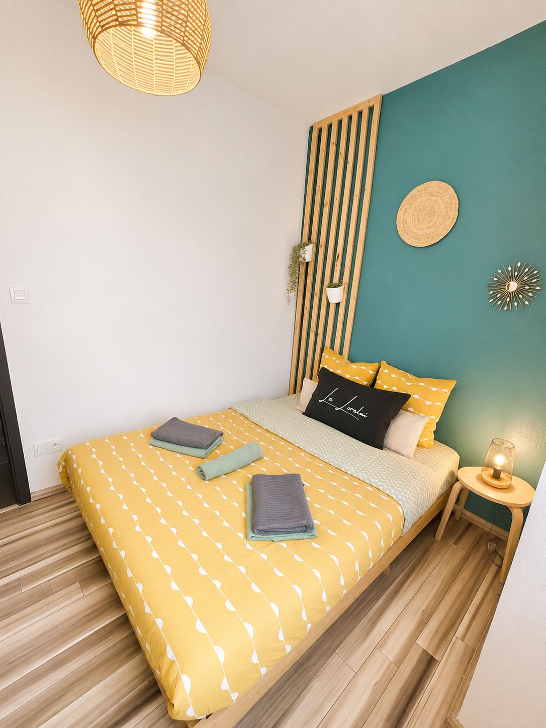 A bedroom with a bed, bedside table, wall-mounted plants, and a hanging light fixture.
