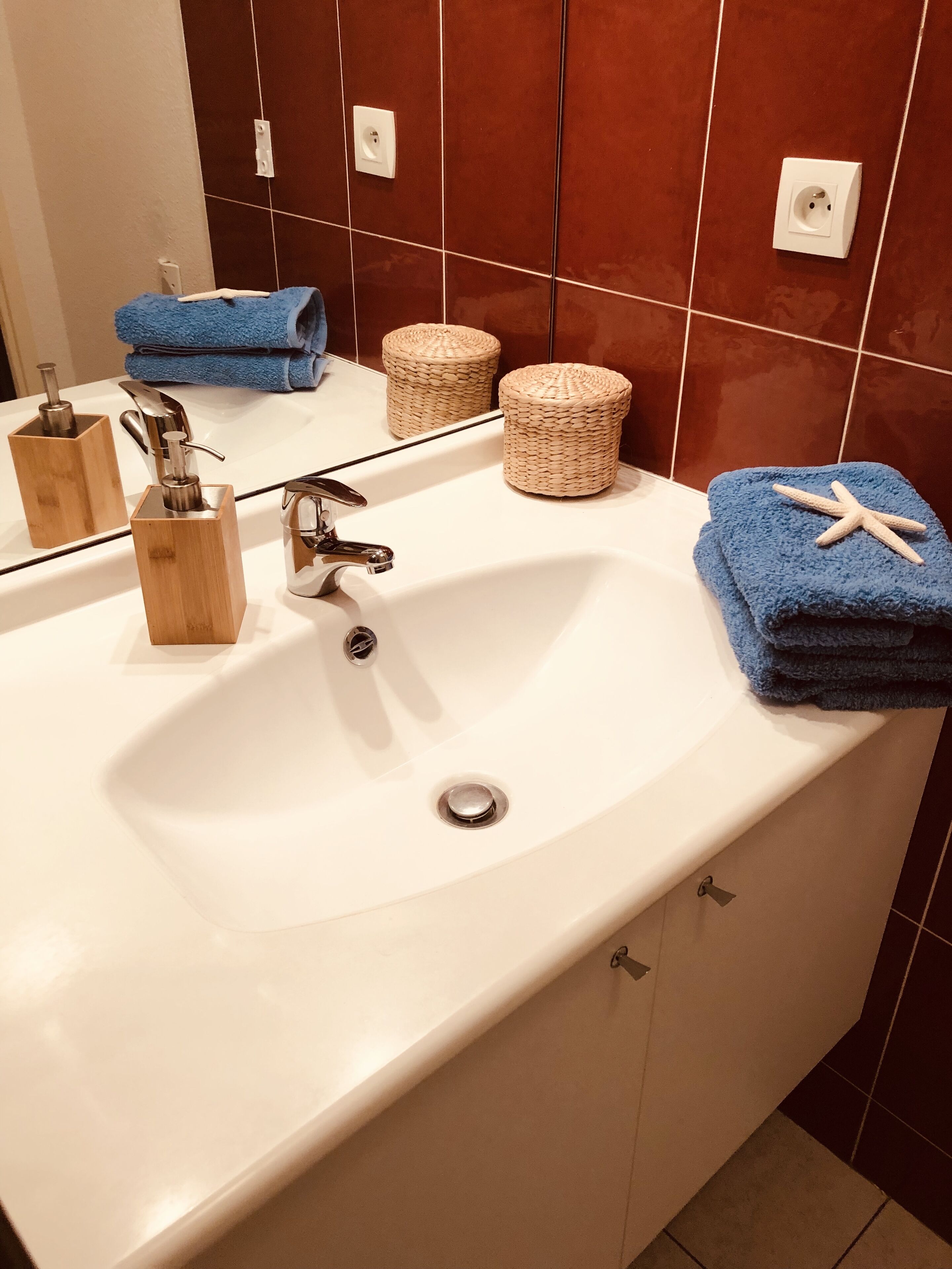 A bathroom with a white sink, wooden soap dispensers, a mirror, and a blue towel with a starfish decoration.